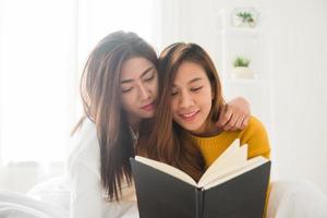 mooie jonge Aziatische vrouwen lgbt lesbische gelukkige paar zittend op bed leesboek samen in de buurt van raam in slaapkamer thuis. LGBT lesbisch koppel samen binnenshuis concept. leuke tijd thuis doorbrengen. foto