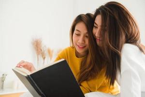 mooie jonge Aziatische vrouwen lgbt lesbische gelukkige paar zittend op bed leesboek samen in de buurt van raam in slaapkamer thuis. LGBT lesbisch koppel samen binnenshuis concept. leuke tijd thuis doorbrengen. foto