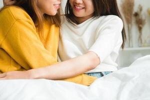 mooie jonge Aziatische vrouwen lgbt lesbische gelukkige paar zittend op bed knuffelen en lachend samen in de slaapkamer thuis. LGBT lesbisch koppel samen binnenshuis concept. leuke tijd thuis doorbrengen. foto