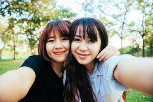 twee mooie gelukkige jonge aziatische vrouwenvrienden die samen plezier hebben in het park en een selfie nemen. gelukkige hipster jonge Aziatische meisjes glimlachen en kijken naar de camera. levensstijl en vriendschap concepten. foto