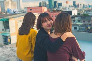 gelukkige groep aziatische vriendinnen genieten en arm omhoog ontspannen pose op dakfeest bij avondzonsondergang, feestelijke vakantieviering, tienerlevensstijl, vrijheid en plezier foto