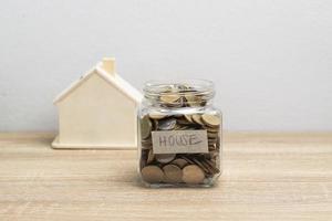 munt in een glazen pot en wit houten huis op de bruine tafel foto