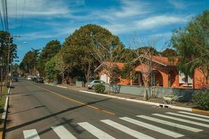 gramado, brazilië - 21 juli 2019. tuinhuizen en bomen op lege geplaveide straat met geparkeerde auto's op een zonnige dag in gramado. een schattig stadje met Europese invloeden, zeer gewild bij toeristen. foto