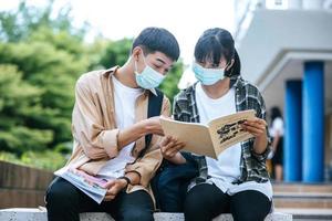 mannelijke en vrouwelijke studenten met maskers zitten en lezen boeken op de trap