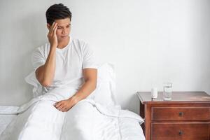 migraine man, hand aanraken van hoofd, zittend in bed. foto