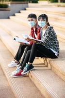mannelijke en vrouwelijke studenten met maskers zitten en lezen boeken op de trap