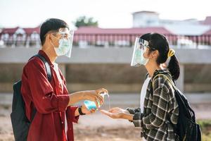 mannelijke en vrouwelijke studenten dragen maskers en knijpen in de gel om hun handen te wassen. foto