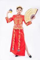 vrouw draagt cheongsam-pak houd de chinese handventilator vast en laat zien dat de creditcard kan worden gebruikt op een evenement in het chinees nieuwjaar