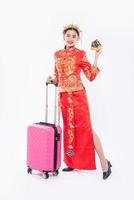 vrouw draagt cheongsam-pak met kroon bereid roze reistas en creditcard voor op reis in chinees nieuwjaar foto