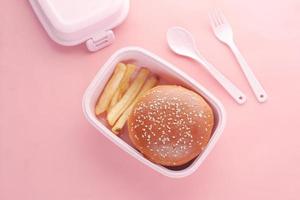 beef burger en franse vriend in een lunchbox op roze achtergrond foto
