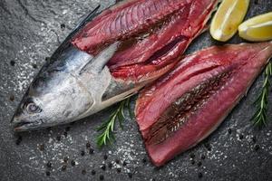 verse visfilet gesneden voor biefstuk of salade met kruiden kruiden rozemarijn en citroen rauwe vis zeevruchten op zwarte plaat achtergrond longtail tonijn, oostelijke kleine tonijnfilet ingrediënten voor het koken van voedsel foto