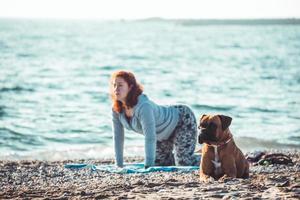 meisje doet yoga en strekt zich uit op het strand met haar hond foto