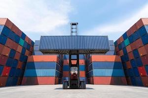 vorkheftruck die vrachtcontainer opheft in de scheepvaartwerf voor import, export, logistiek industrieel met containerstapelachtergrond foto