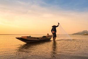 Aziatische visser die een net gooit voor het vangen van zoetwatervissen in de natuurrivier in de vroege ochtend voor zonsopgang foto