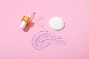 druppelaar en druppels olie of serum, uitstrijkje van crème, gel op roze oppervlak - cosmetica en verzorgingsproducten voor spa's bovenaanzicht foto