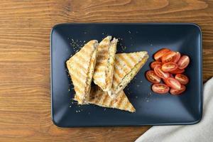 krokante geroosterde sandwiches met kaas en tomaten op een zwarte plaat. foto