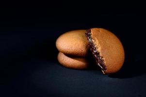 koekjes gevuld met chocoladeroom. chocolade crème koekjes. bruine chocoladekoekjes met roomvulling op zwarte achtergrond. foto