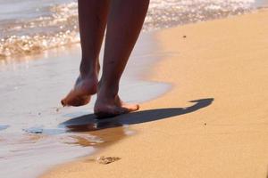 vrouw die blootsvoets op het zand loopt en voetstappen op het gouden strand achterlaat. vrouwelijke benen lopen door de zee. concept van vakantie, zomervakantie of vakantie. foto