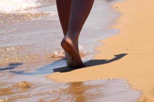 vrouw die blootsvoets op het zand loopt en voetstappen op het gouden strand achterlaat. vrouwelijke benen lopen door de zee. concept van vakantie, zomervakantie of vakantie. foto