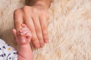 vader houdt een kleine babyhand in zijn handen. kleine hand van een pasgeboren baby in grote handen van papa. baby houdt vaders vinger vast