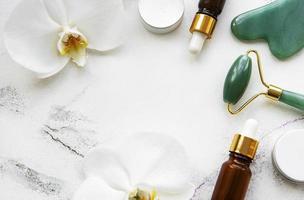 gezichtsmassage jade roller met cosmetisch product op witte marmeren achtergrond foto
