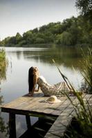 ontspannende jonge vrouw op houten pier aan het meer foto
