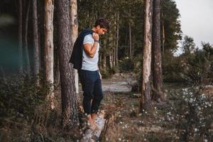 knappe man die buiten in het bos poseert, staat blootsvoets op een boomstam, gekleed in een geruit jasje. plaats voor tekst of reclame foto