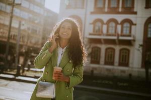 jonge vrouw die smartphone op straat gebruikt en afhaalkoffie houdt foto