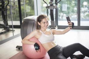 mooie Aziatische sportvrouw speelt slimme telefoon in de sportschool foto