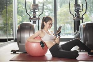 mooie Aziatische sportvrouw speelt slimme telefoon in de sportschool foto