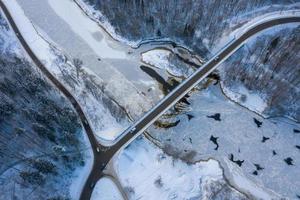 winterseizoen luchtfoto van boven naar beneden uitzicht op een brug met een rechte lijnweg over de rivier
