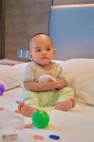 portret van een gelukkige 6 maanden oude Aziatische babyjongen die op bed zit te spelen foto