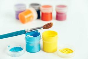 kleurrijke gouacheverf en penseel om op witte houten tafel te schilderen. kopiëren, lege ruimte voor tekst foto