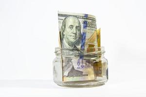 bankbiljetten van verschillende valuta in een glazen pot op een witte achtergrond. foto