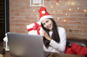 jonge lachende vrouw met rode kerstman hoed video bellen op sociaal netwerk met familie en vrienden op eerste kerstdag.