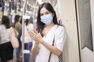 een jonge vrouw met een beschermend masker in de metro gebruikt alcohol om handen te wassen, reist onder covid-19 pandemie, veiligheidsreizen, protocol voor sociale afstand, nieuw normaal reisconcept foto