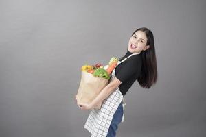 portret van mooie jonge vrouw met groenten in boodschappentas in studio grijze achtergrond foto