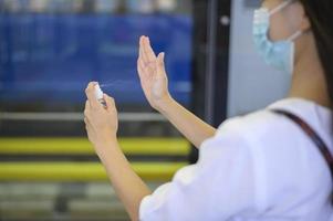 een jonge vrouw met een beschermend masker in de metro gebruikt alcohol om handen te wassen, reist onder covid-19 pandemie, veiligheidsreizen, protocol voor sociale afstand, nieuw normaal reisconcept foto