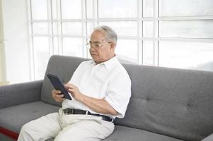 een gelukkige senior aziatische man gebruikt tablet en praat met familie op webcam thuis, pensioenconcept. foto