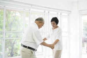 vrolijk senior aziatisch gepensioneerd echtpaar danst en geniet van de muziek in de woonkamer thuis, gezondheidsconcept
