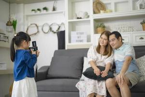 een schattige aziatische dochter die een camera vasthoudt, maakt in het weekend foto's van haar ouders thuis. foto