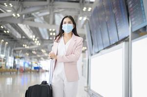 een zakenvrouw draagt een beschermend masker op de internationale luchthaven, reist onder covid-19 pandemie, veiligheidsreizen, protocol voor sociale afstand, nieuw normaal reisconcept foto