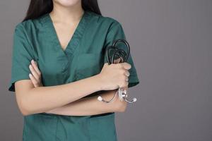 een vrouwelijke arts die een groene scrub en een stethoscoop draagt, is op een grijze achtergrondstudio foto