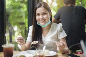 jonge vrouw met gezichtsmasker heeft eten in restaurant, nieuw normaal concept. foto