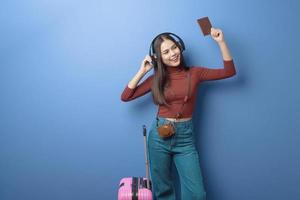 portret van jonge gelukkige mooie vrouw luistert naar muziek en reist aan boord met paspoort over geïsoleerde blauwe achtergrondstudio foto