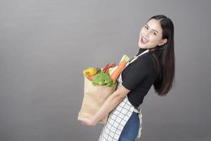 portret van mooie jonge vrouw met groenten in boodschappentas in studio grijze achtergrond foto