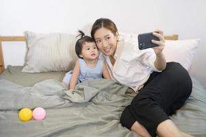 Aziatische moeder en haar dochtertje maken selfie of videogesprek met vader in bed, familie, veiligheid thuis, ouderschap, technologieconcept foto