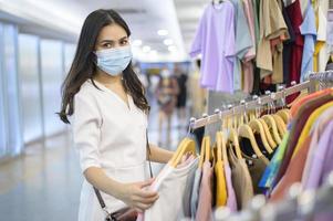 vrouw met gezichtsmasker winkelt kleren in het winkelcentrum foto