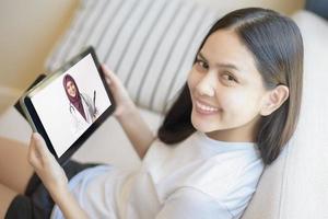 tabletmonitor uitzicht over meisjesschouder, een moslim arts-vrouw draagt uniform en geeft advies aan jonge vrouwen, concept voor gezondheidszorgtechnologie foto