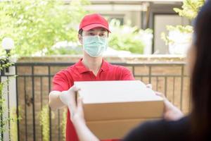 de koeriersman met beschermend masker en handschoenen bezorgt doosvoedsel tijdens een virusuitbraak. veilig thuisbezorgd. foto